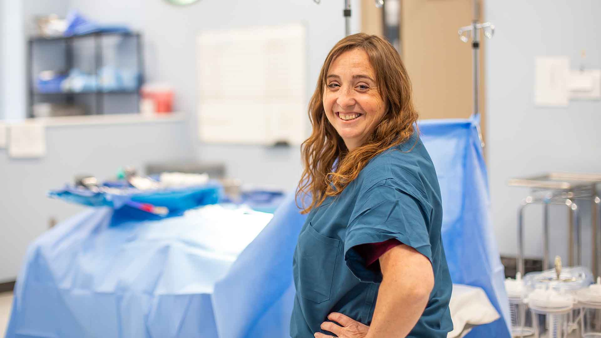 Healthcare professional in scrubs smiling in a hospital operating room.